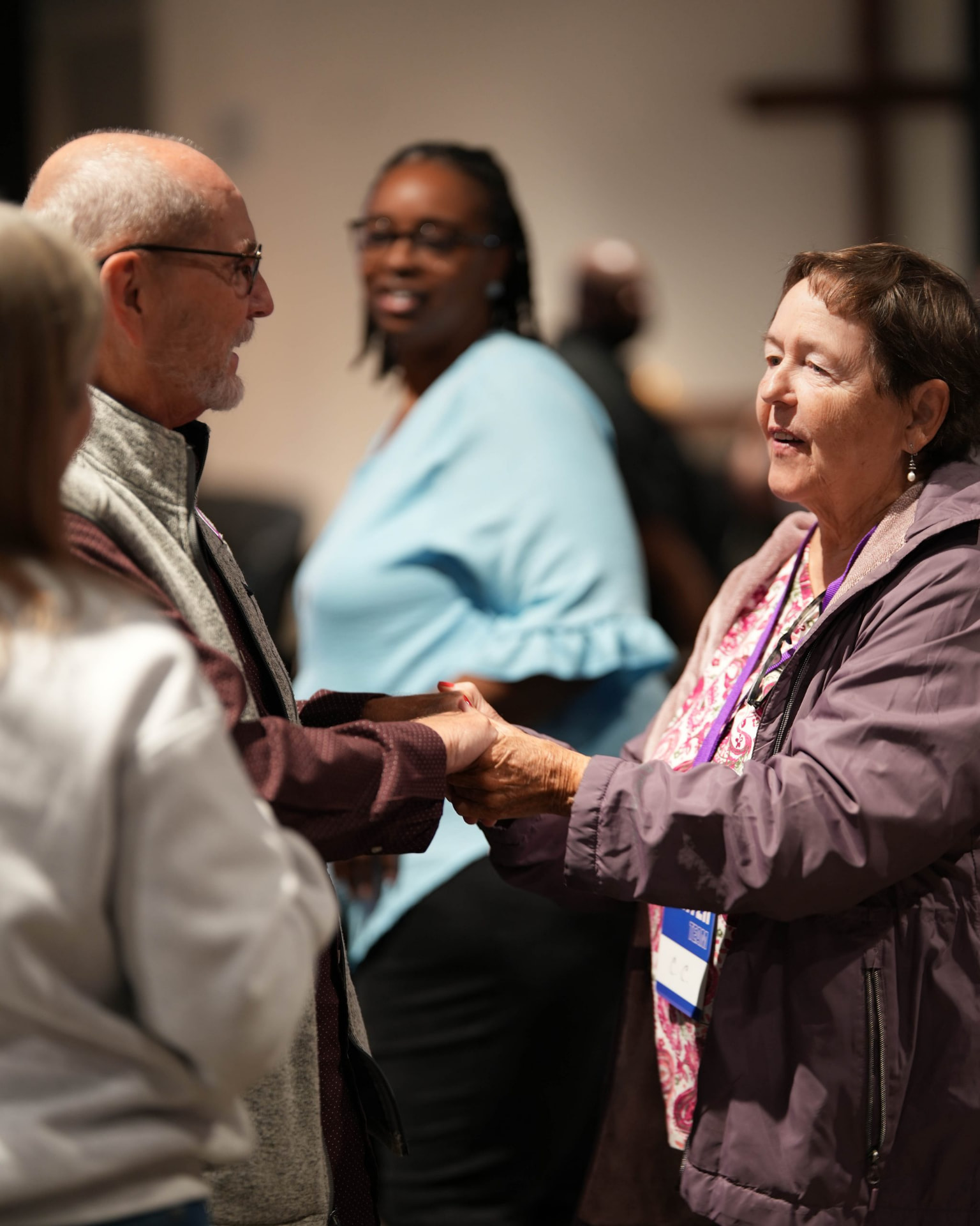 An older man and woman holding hands while talking at an indoor gathering.