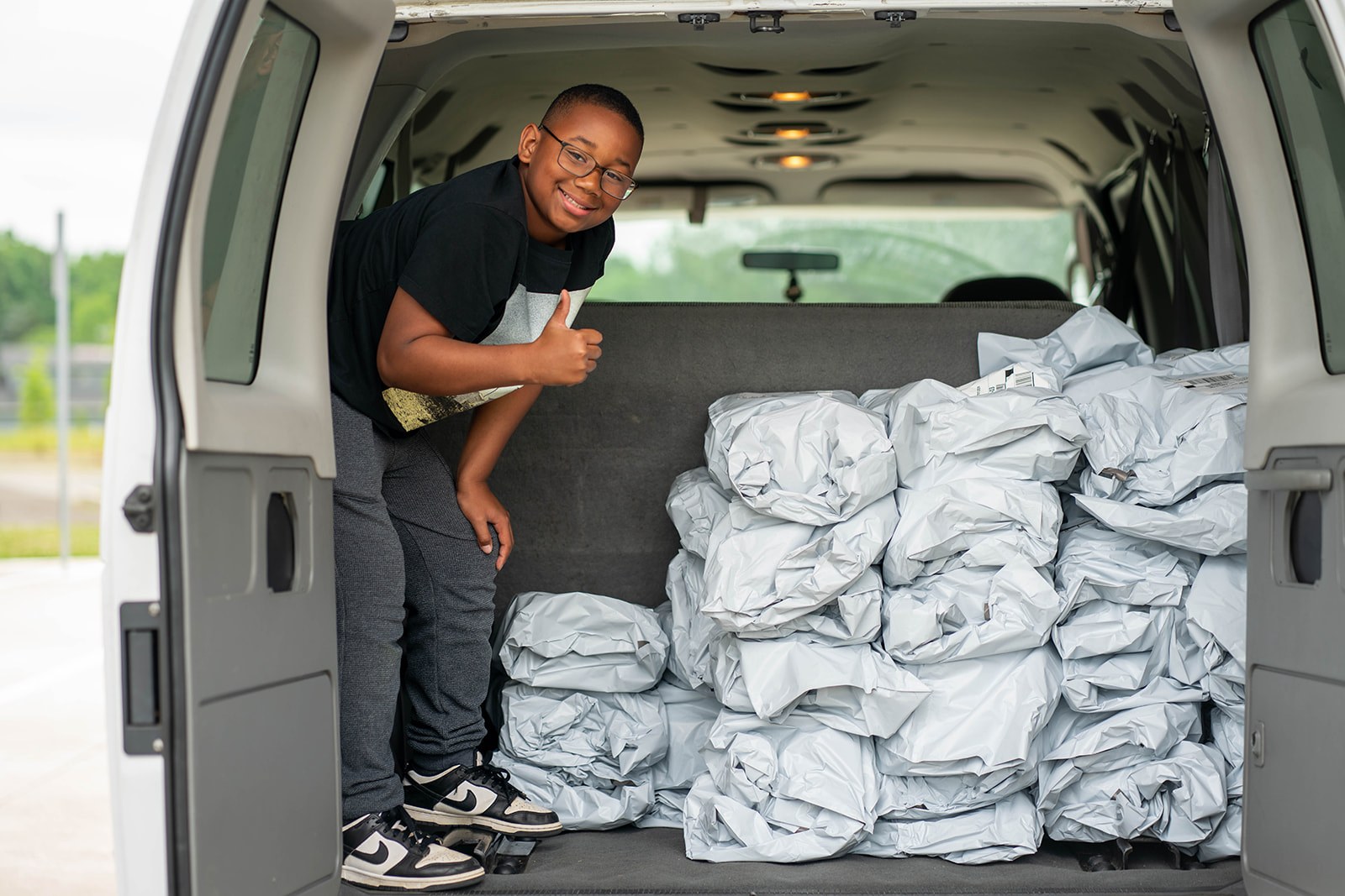 A young volunteer giving a thumbs up while loading donation bags into a van
