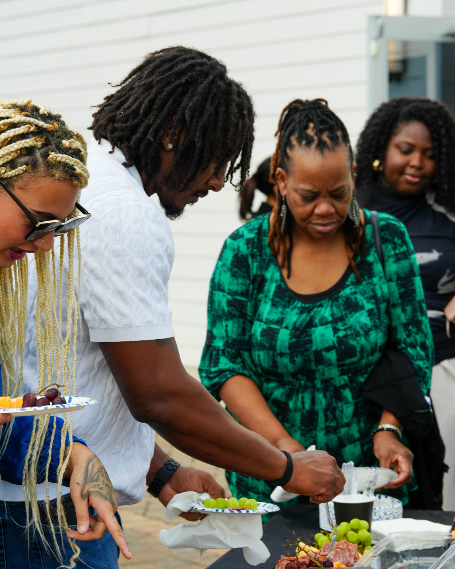 Adults serving themselves fruit and food at an outdoor buffet table.