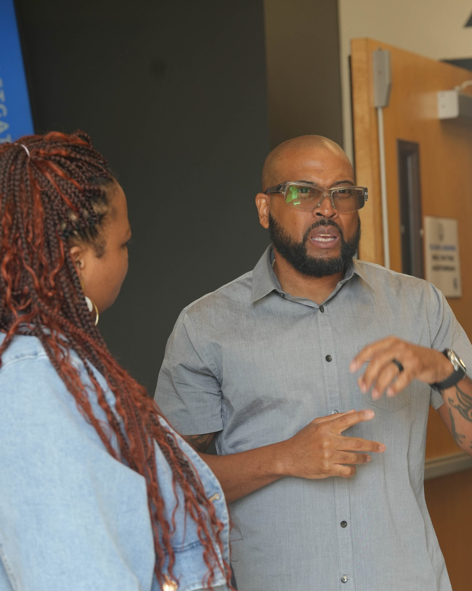 A man gesturing as he talks with a woman in an indoor meeting room.